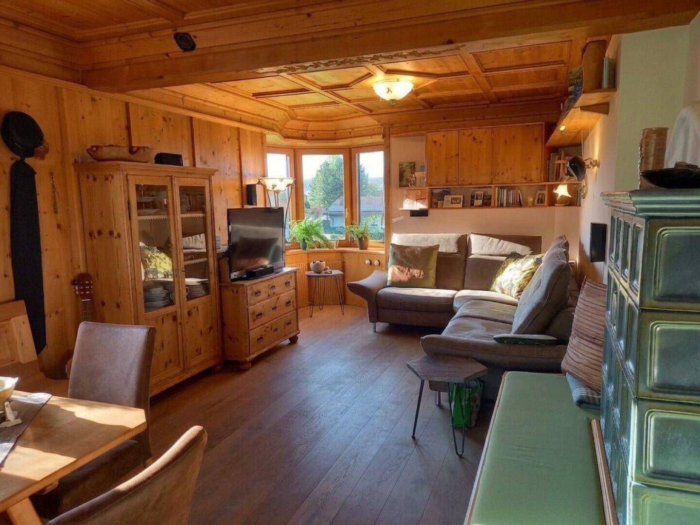 Gemütliches Wohnzimmer im alpinen Stil mit Holzwänden, Kachelofen und großem Erkerfenster.