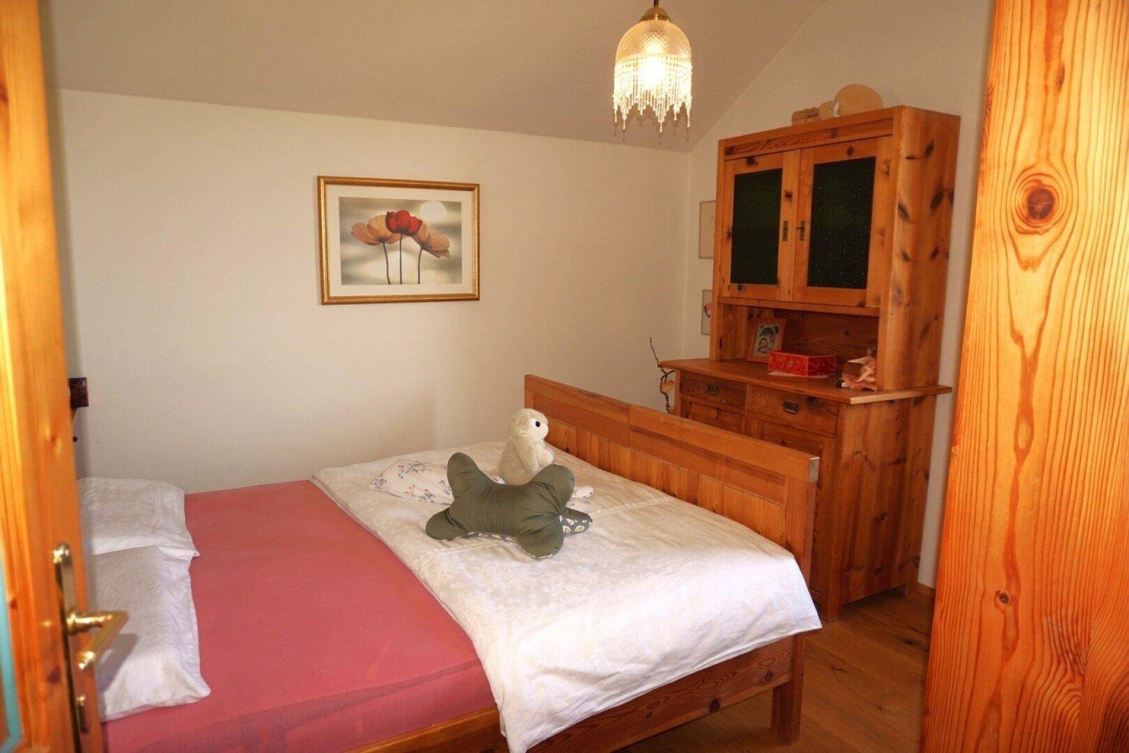 Helles Schlafzimmer mit Holzbett, Schrank und schlichten weißen Wänden, mit Holzboden.