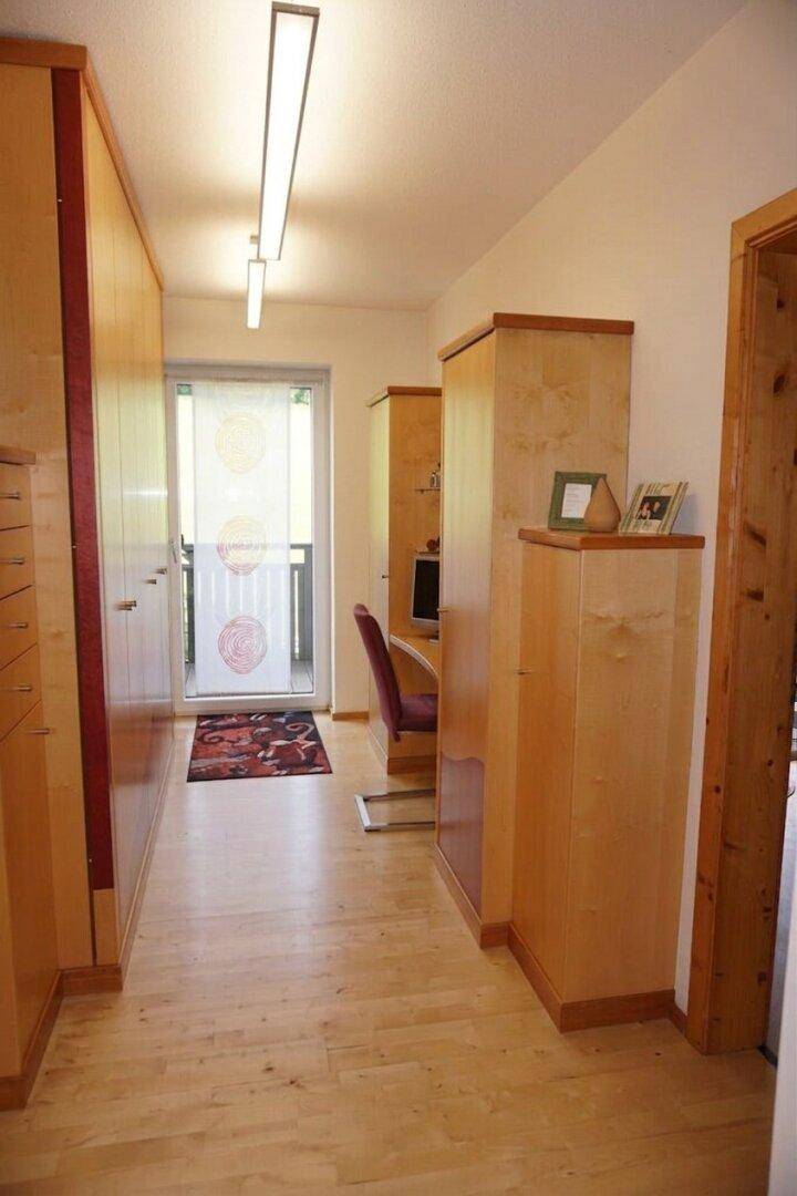 Heller Flur mit Holzschränken, Parkettboden und Zugang zu einem kleinen Balkon.
