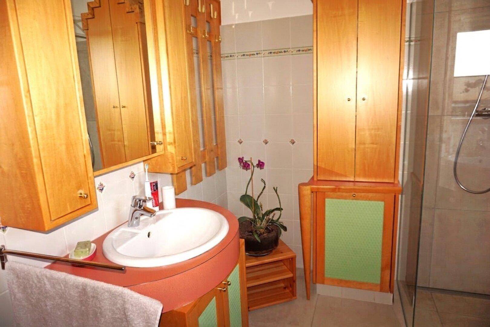 Badezimmer mit Holzschränken, Waschbecken und Duschbereich, funktional und hell.