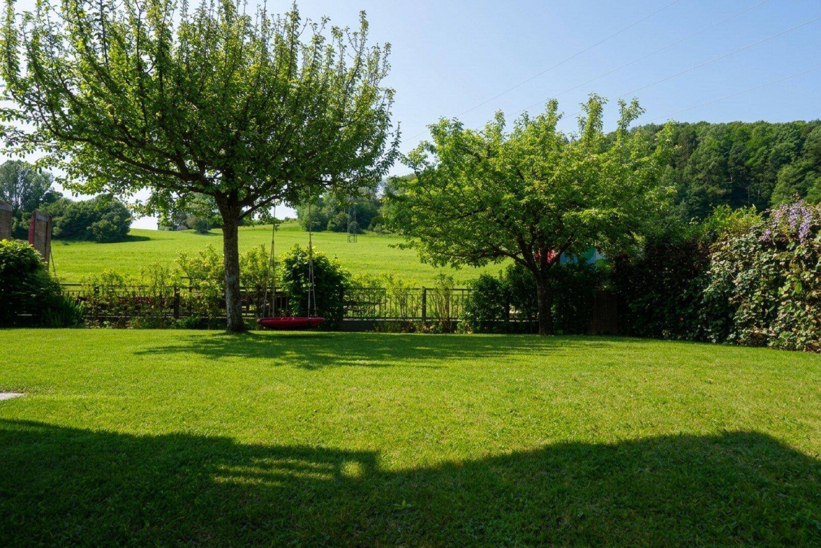 Weitläufiger Garten mit gepflegtem Rasen, Bäumen und idyllischer ländlicher Umgebung.