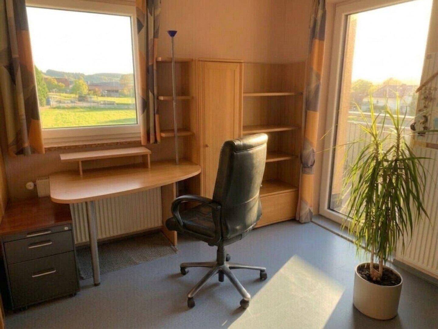 Helles Arbeitszimmer mit Schreibtisch, Regal und großem Fenster mit Blick ins Grüne.