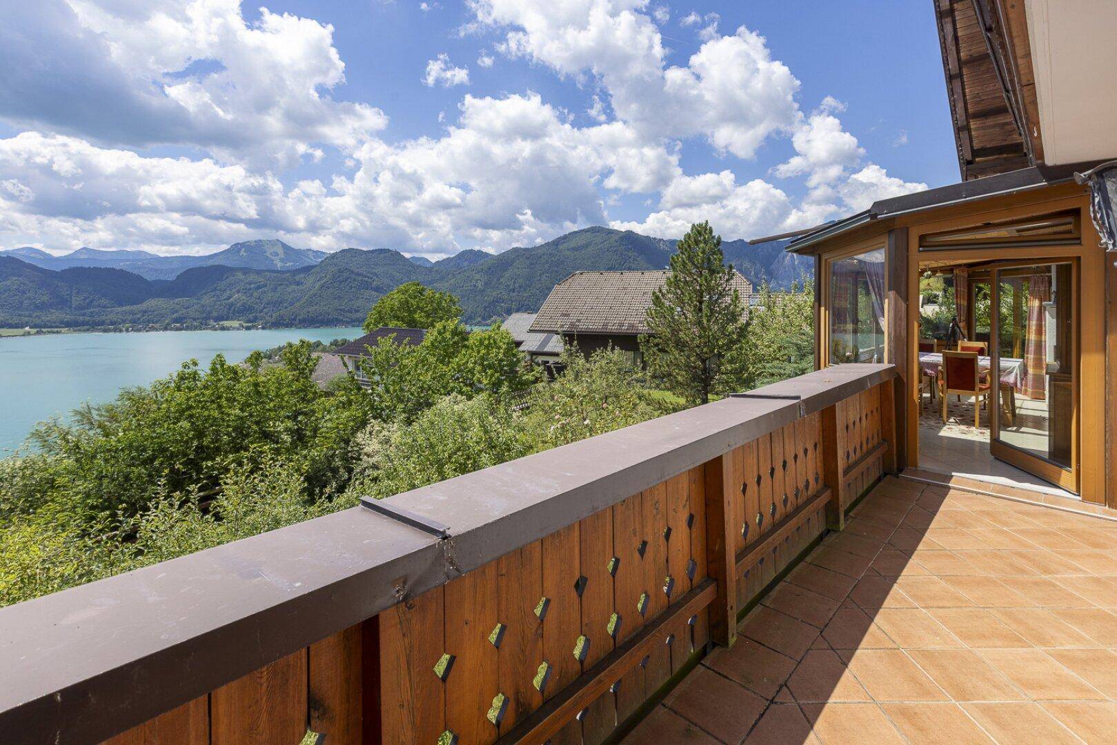Geräumiger Balkon mit Fliesenboden und Holzgeländer, bietet einen weiten Blick auf den See und die Berge.