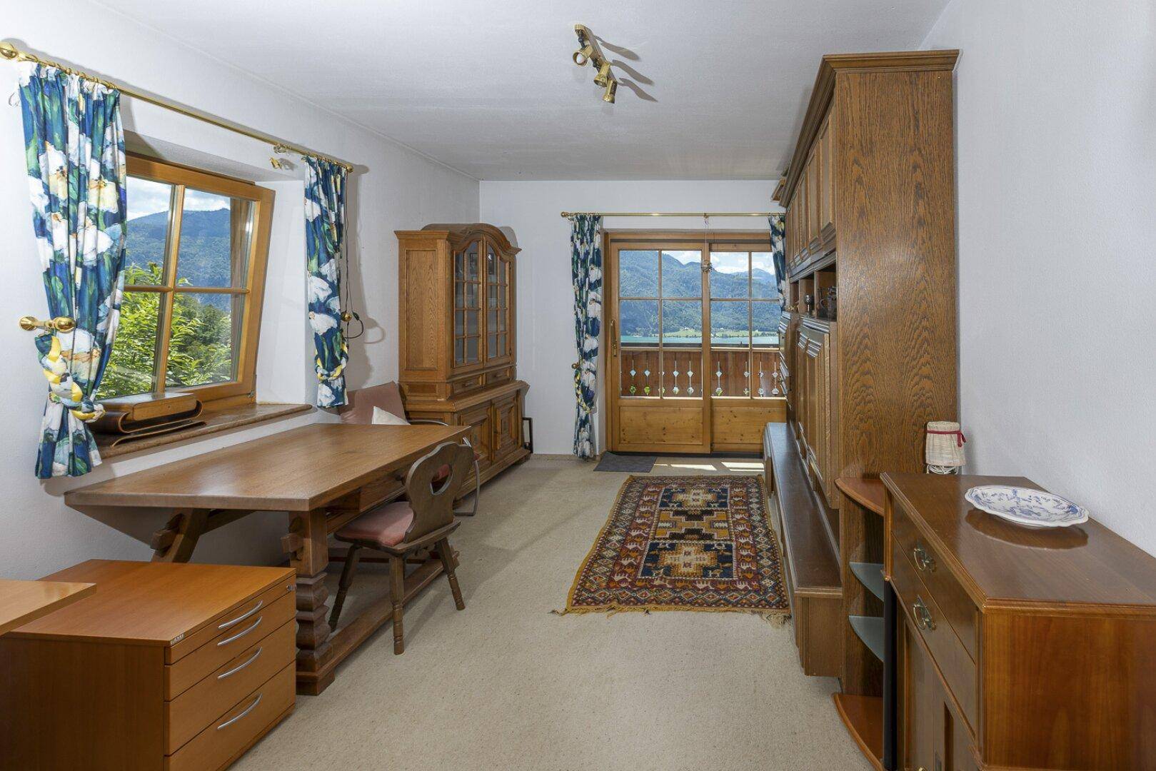 Gemütlicher Raum mit Holztisch, Schränken und Zugang zu einem Balkon mit Bergblick.