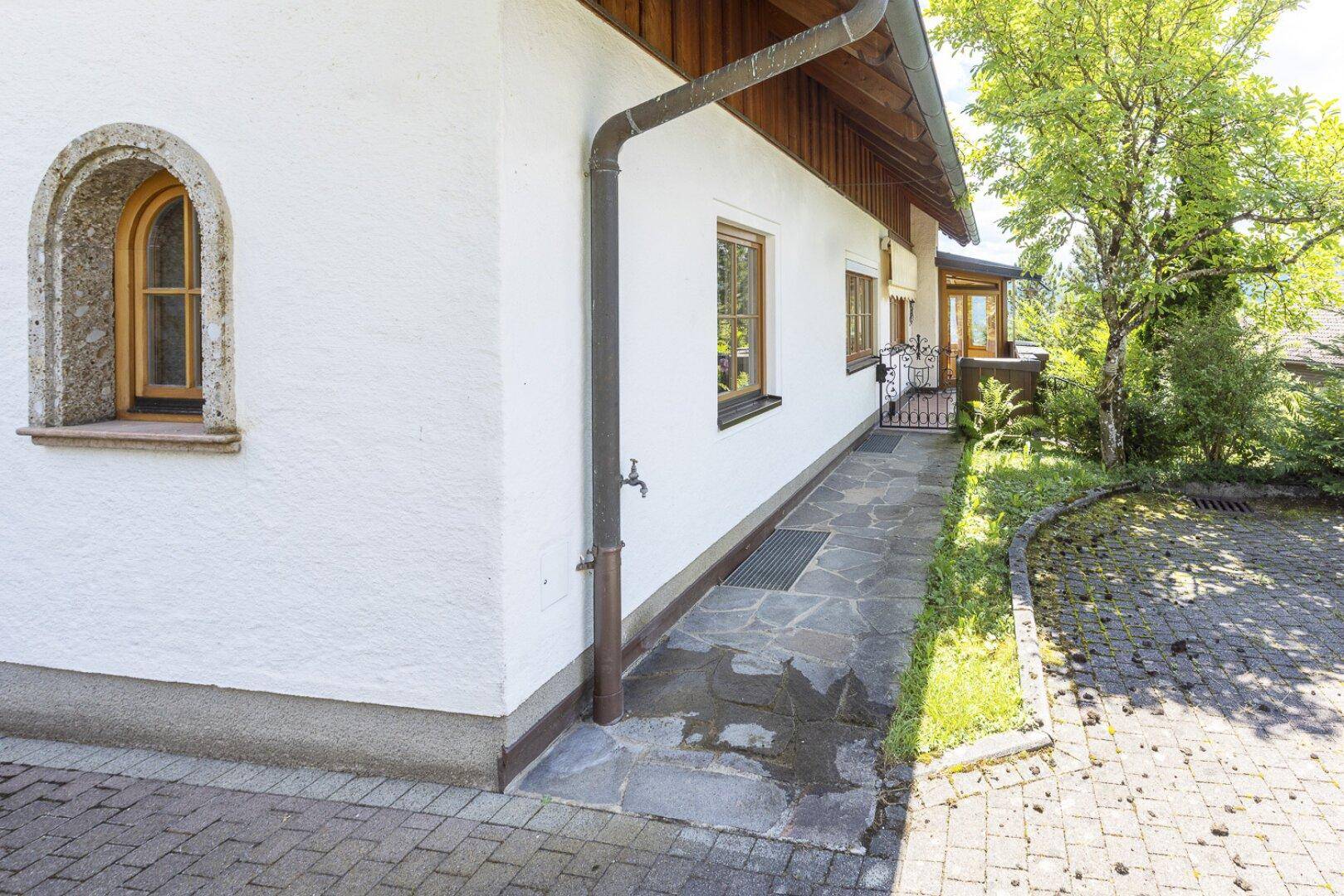 Seitenansicht des Hauses mit weißer Fassade, Holzelementen und gepflastertem Weg im Grünen.