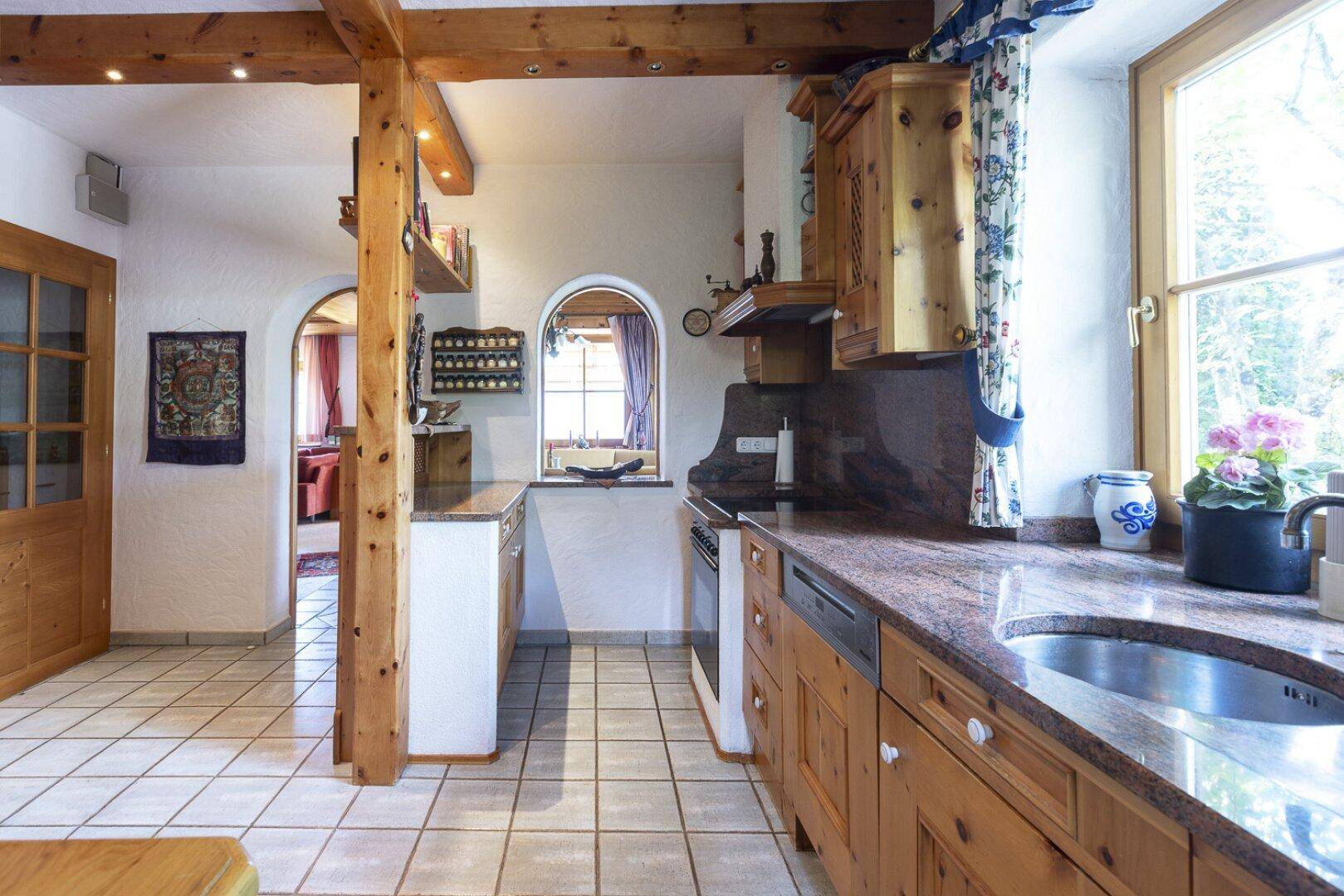 Rustikale Küche mit Holzmöbeln, Granitarbeitsplatten und Fliesenboden, offen zum Wohnbereich.
