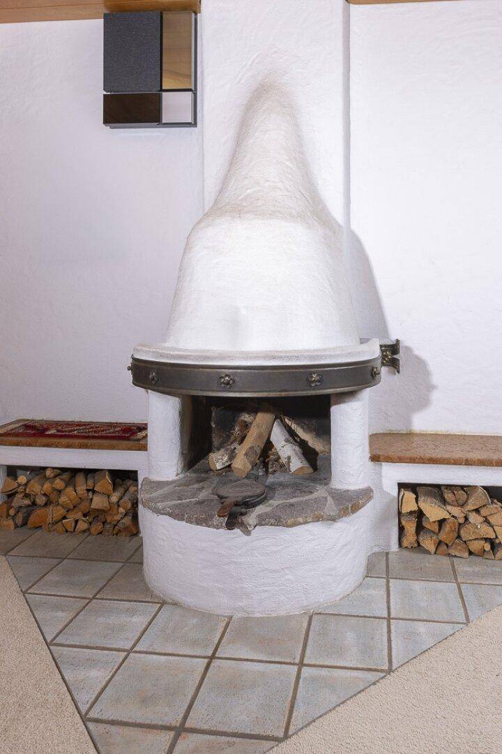 Detailaufnahme eines traditionellen Kaminofens mit Holzscheiten und Fliesenboden.