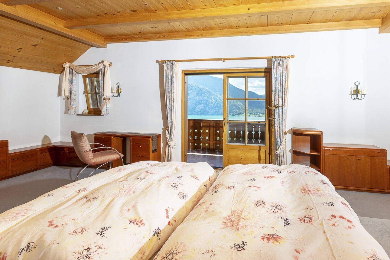 Schlafzimmer mit Doppelbett, Teppichboden und Balkonzugang mit Seeblick.