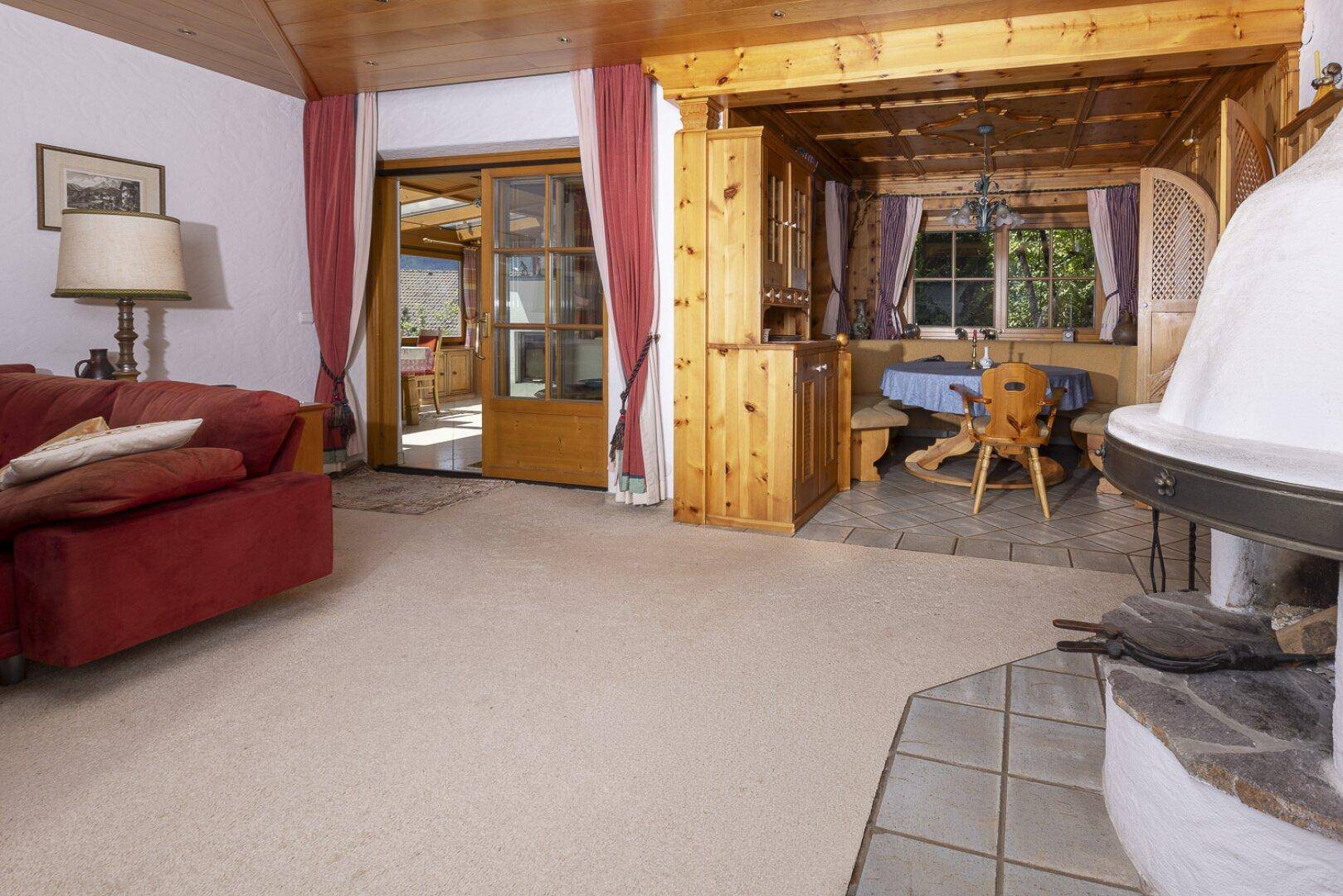 Wohnzimmer mit Teppichboden und Zugang zu einem Essbereich im alpenländischen Stil.