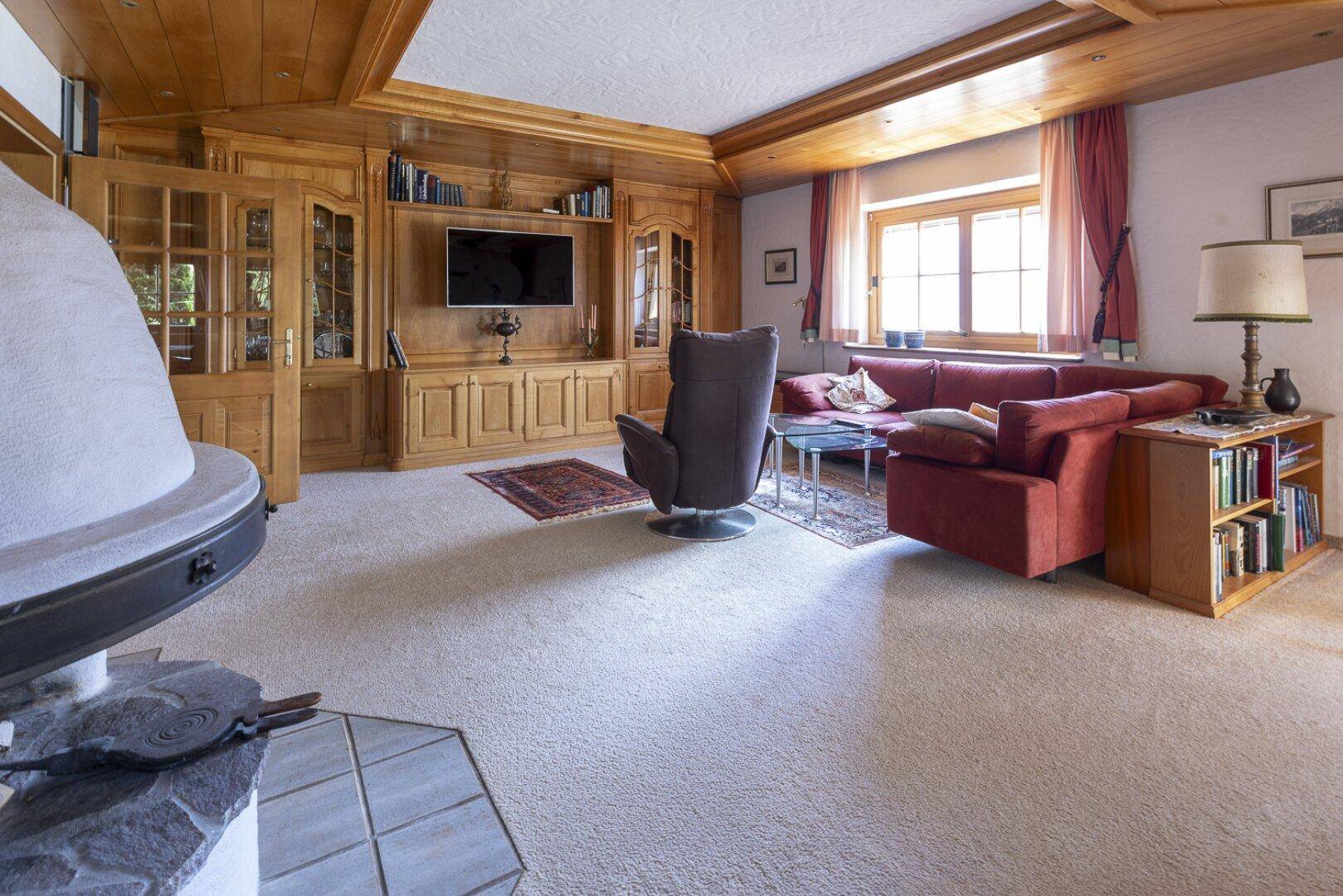 Geräumiges Wohnzimmer mit Teppichboden, Holzeinbauten und einem Kaminofen.