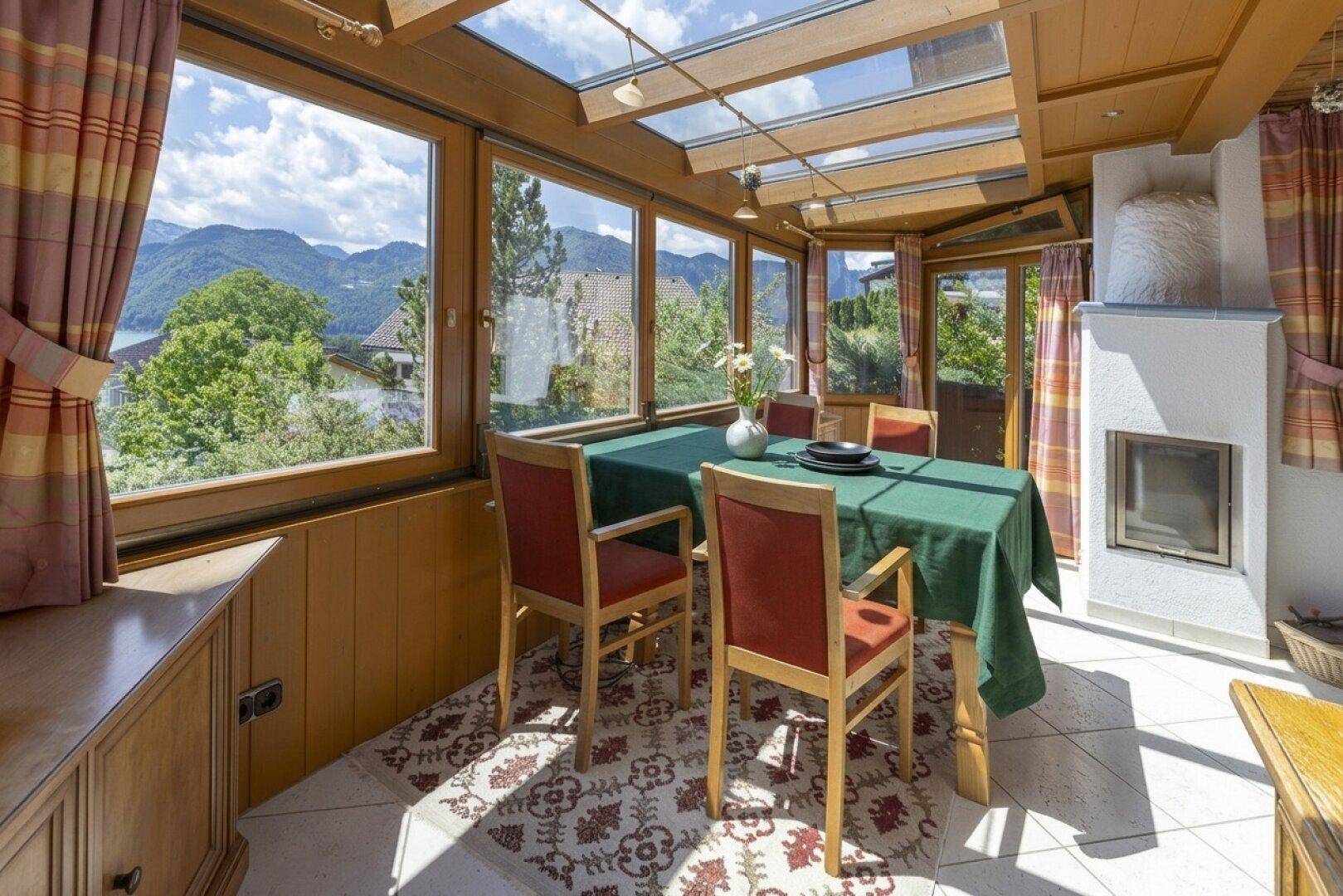 Gemütlicher Wintergarten mit Esstisch, Kamin und weitem Blick auf die umliegende Natur und den See.