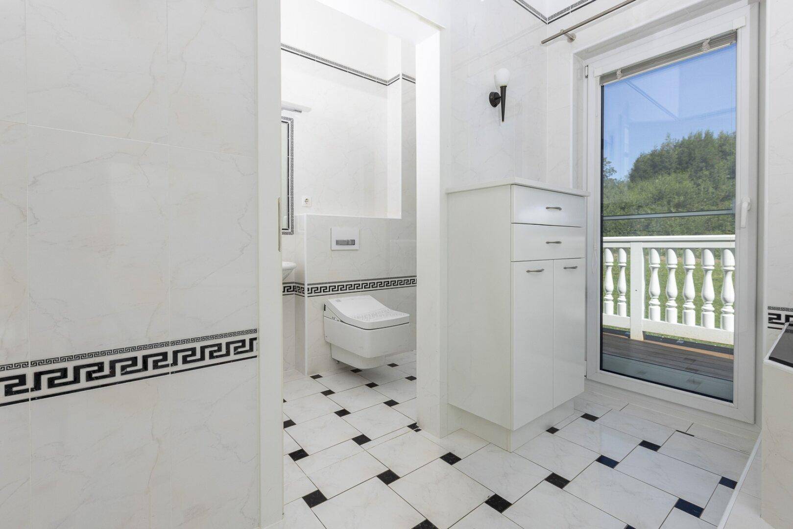 Helles Badezimmer mit wandhängendem WC, Fliesenboden und direktem Zugang zu einem Balkon.
