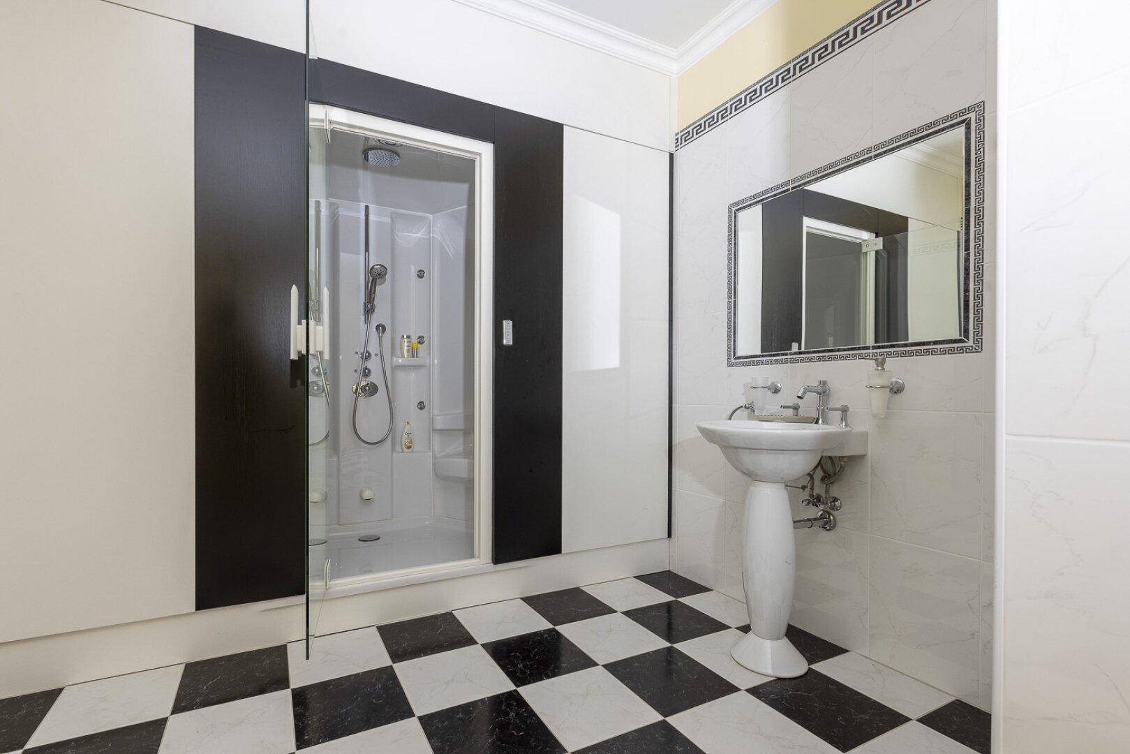Elegantes Badezimmer mit Duschkabine, Standwaschbecken und markantem schwarz-weißem Fliesenmuster.