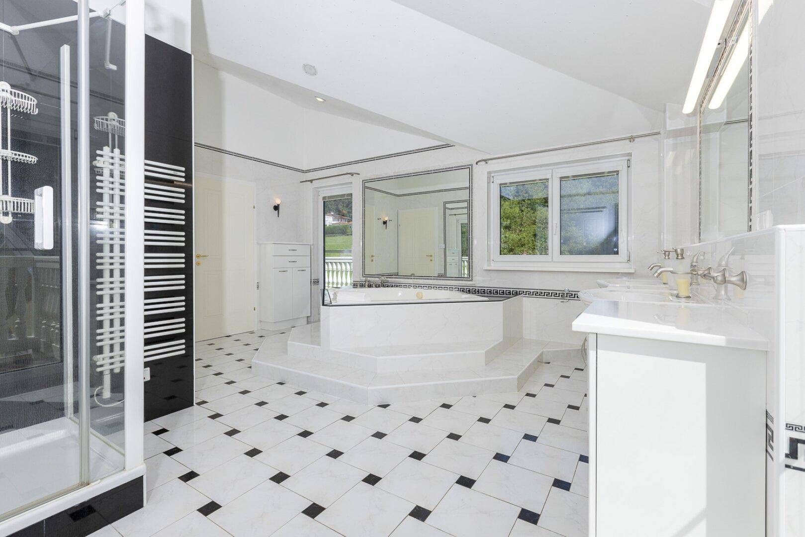 Geräumiges Badezimmer mit großer Badewanne, Dusche und schwarz-weiß kariertem Fliesenboden.