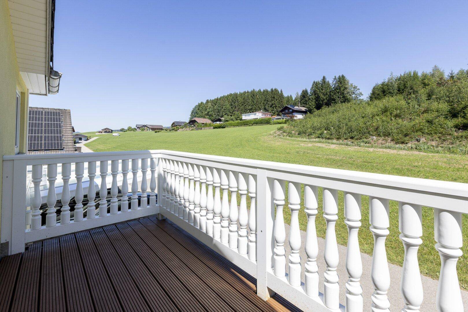 Kleiner Balkon mit Holzboden und weißem Geländer, bietet einen Blick auf die grüne Umgebung.