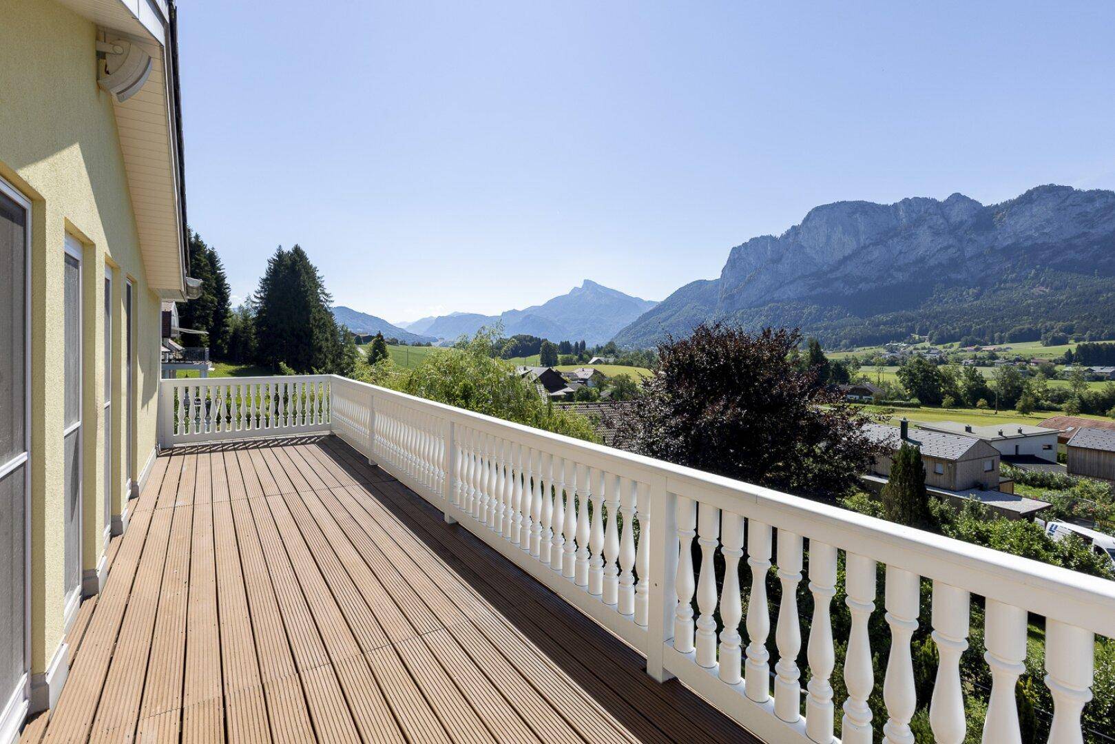 Geräumiger Balkon mit Holzboden und weißem Geländer, bietet einen weiten Blick auf die umliegende Berglandschaft.