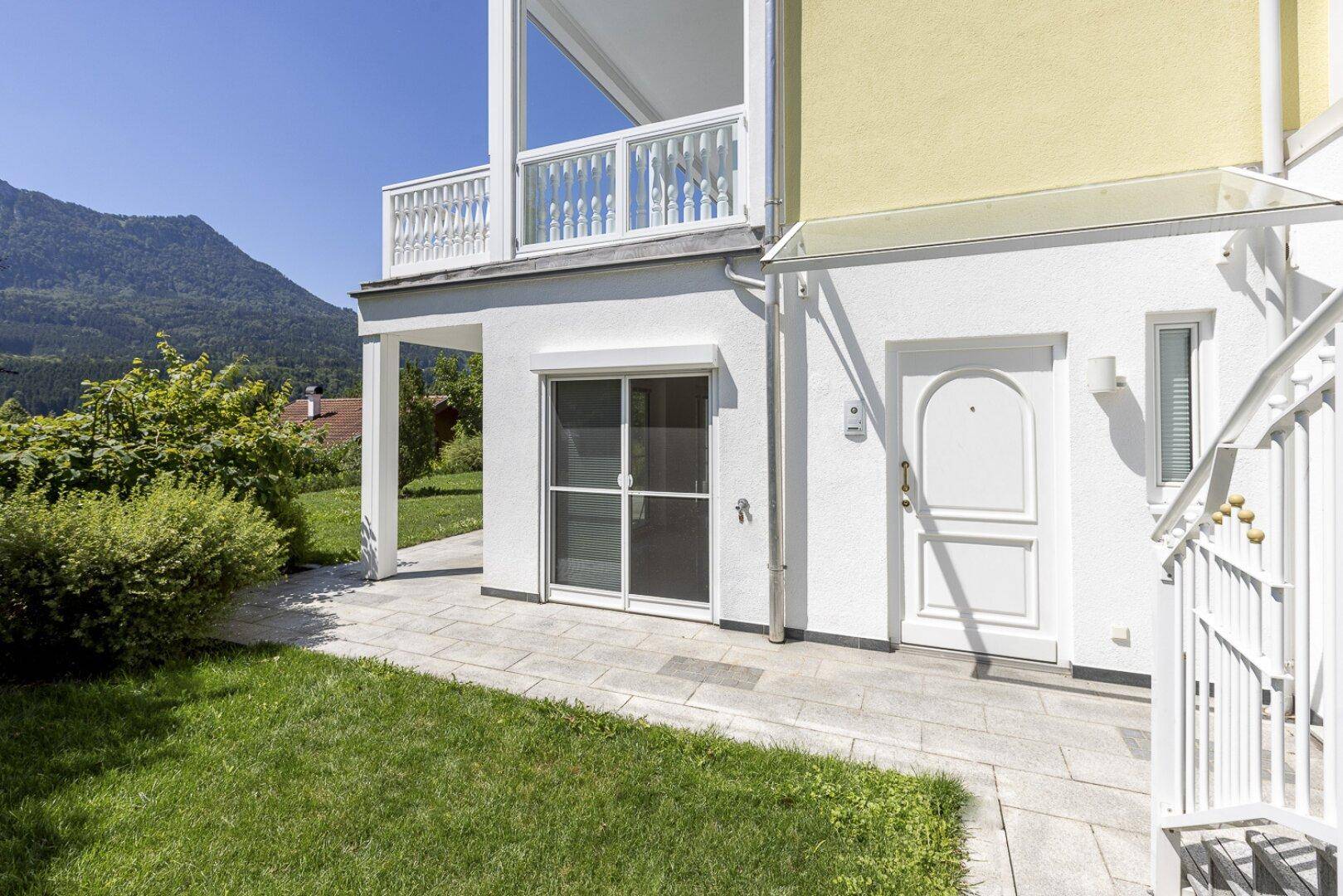 Eingangsbereich mit gepflastertem Patio und Zugang zum Garten, umgeben von grüner Landschaft.