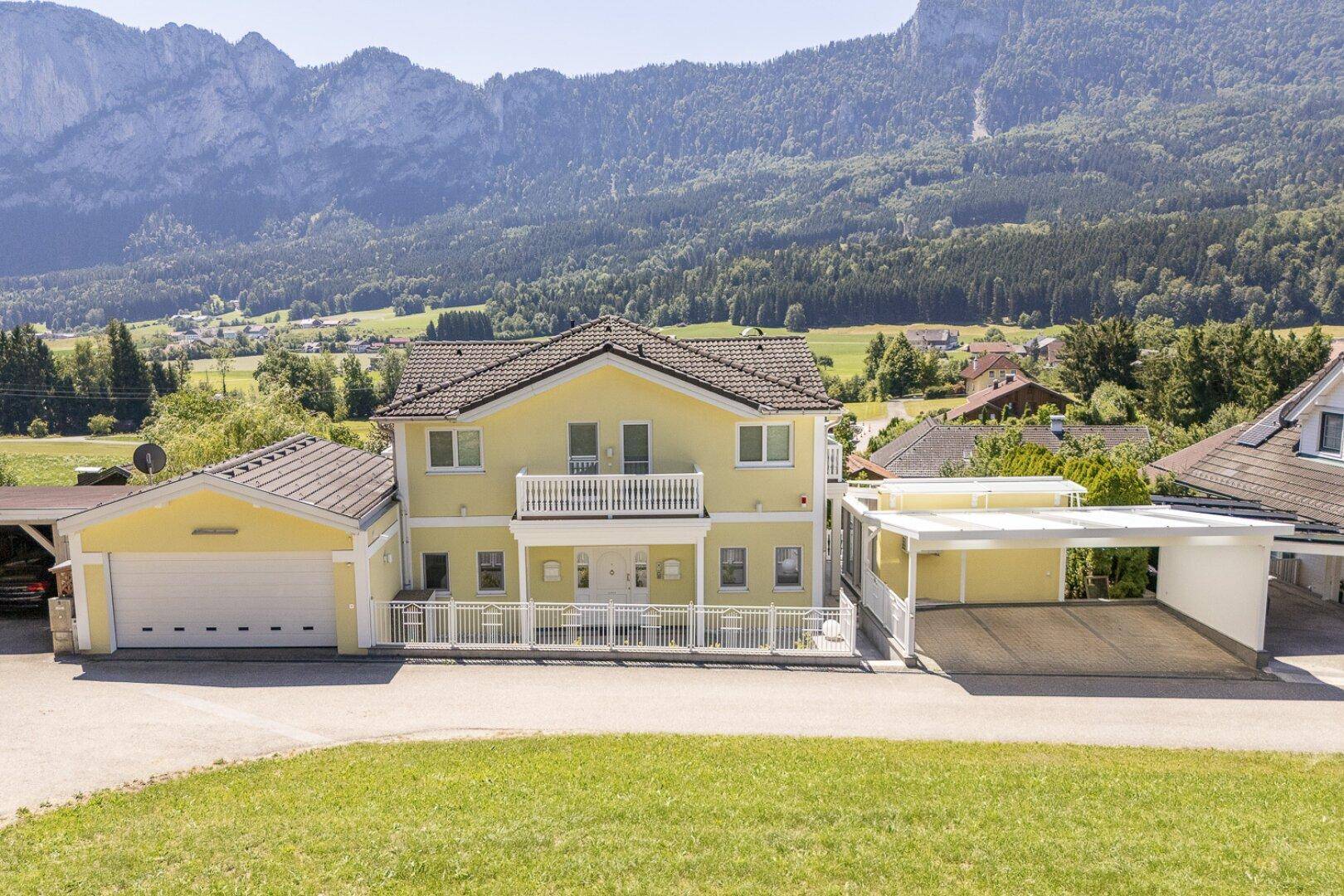 Gesamtansicht des Hauses mit Garage, Carport und beeindruckendem Bergpanorama im Hintergrund.