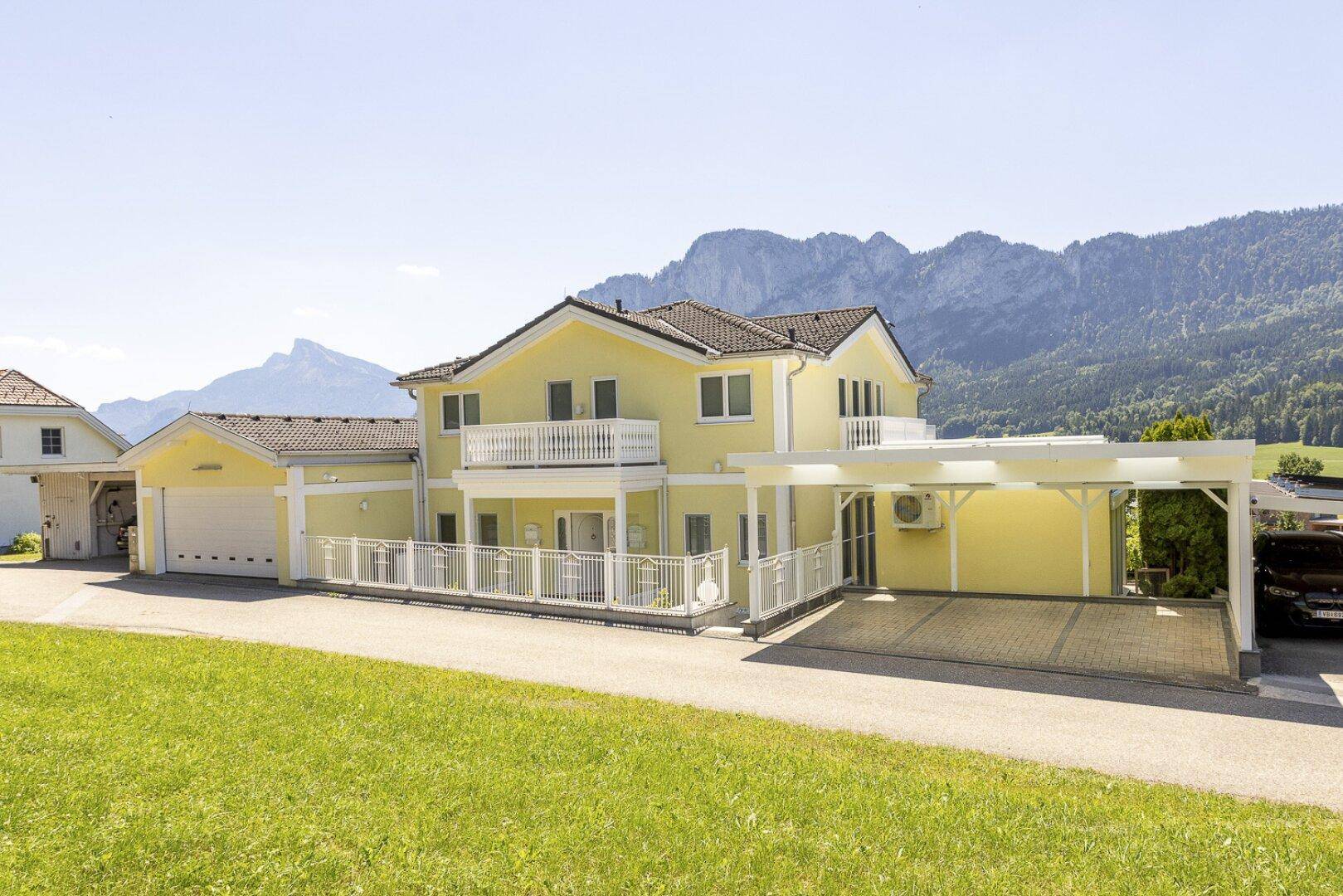 Ansicht des Hauses mit integrierter Doppelgarage und einem zusätzlichen Carport, umgeben von Natur.