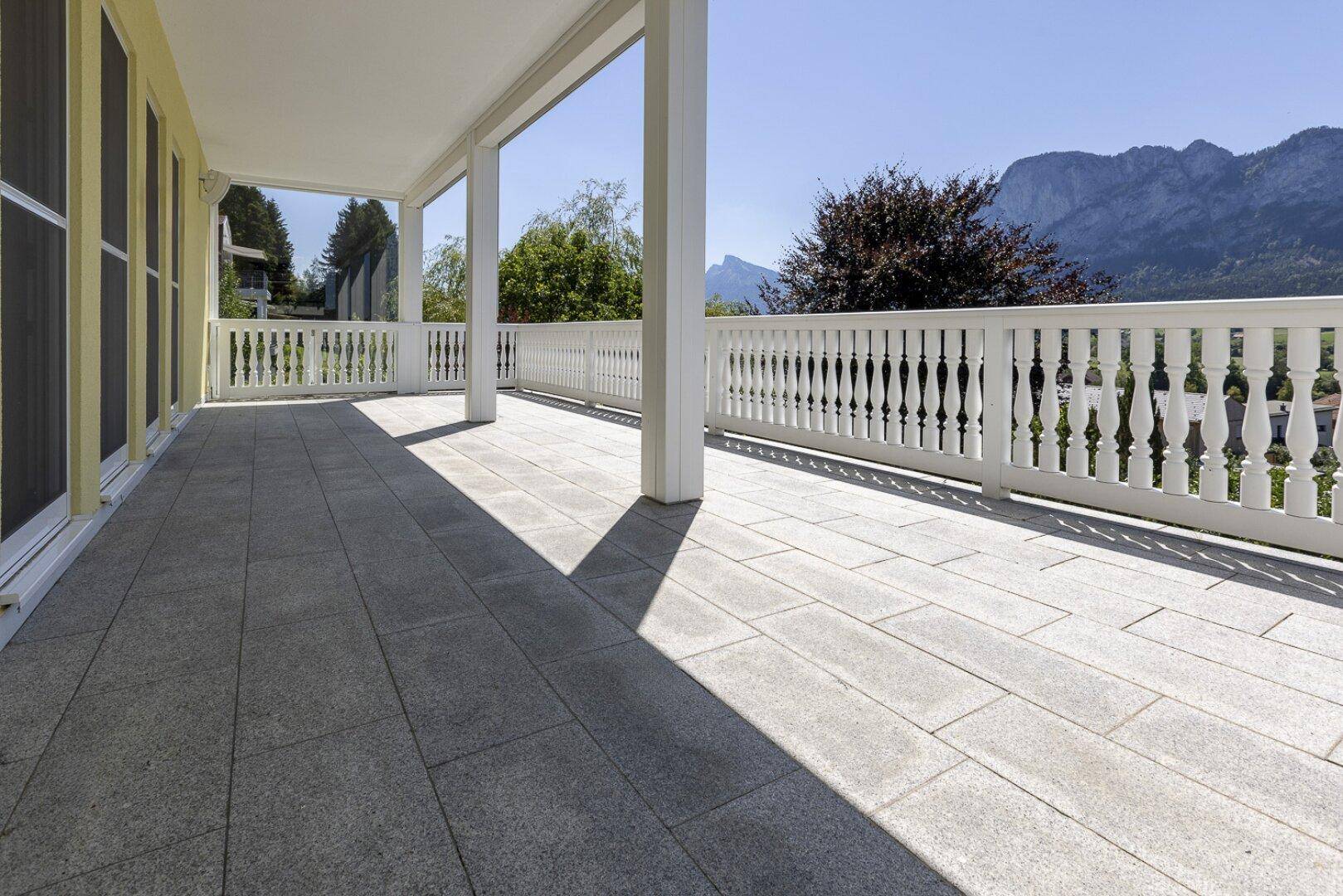 Geräumige Terrasse mit Fliesenboden, weißem Geländer und weitem Bergblick unter blauem Himmel.