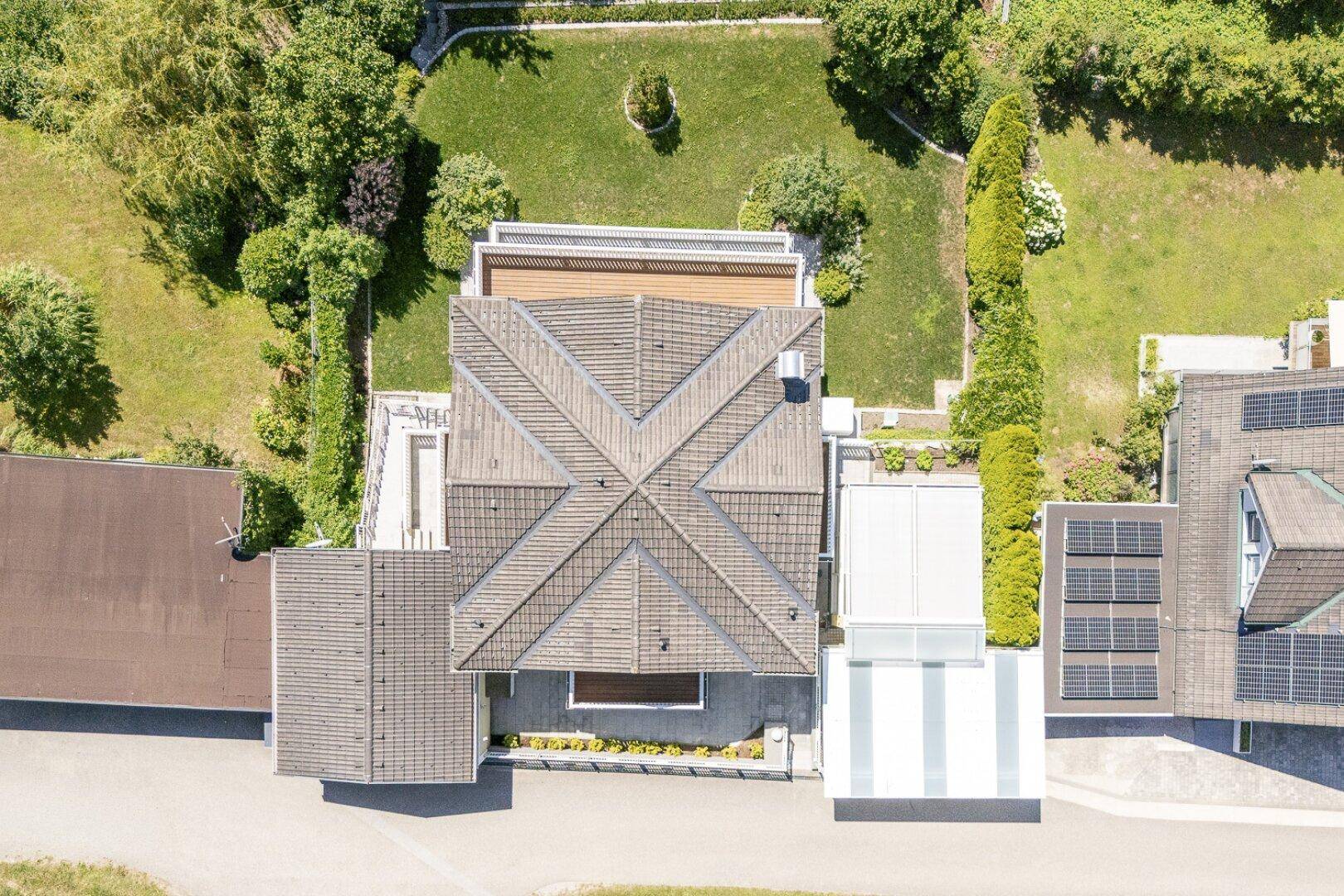 Luftaufnahme des Anwesens mit Satteldach, gepflegtem Garten und angrenzenden Gebäuden mit Solaranlagen.