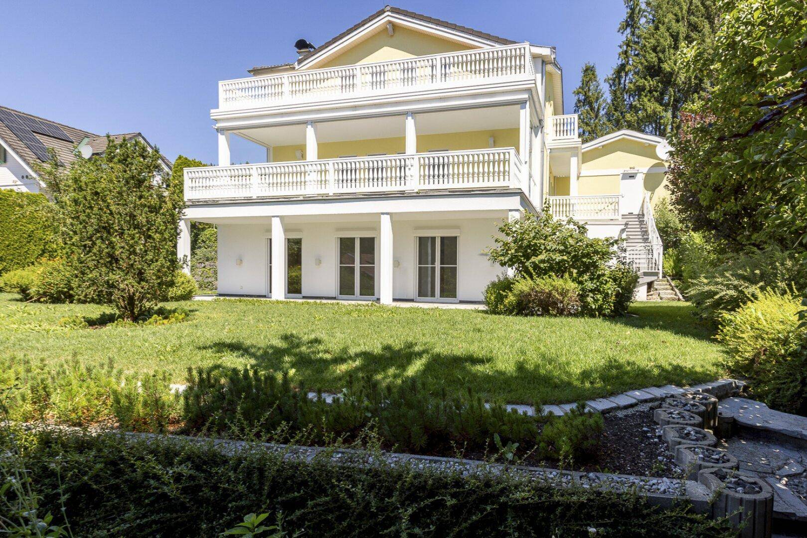 Elegantes Haus mit gelber Fassade, mehreren Balkonen und einem weitläufigen, gepflegten Gartenbereich.