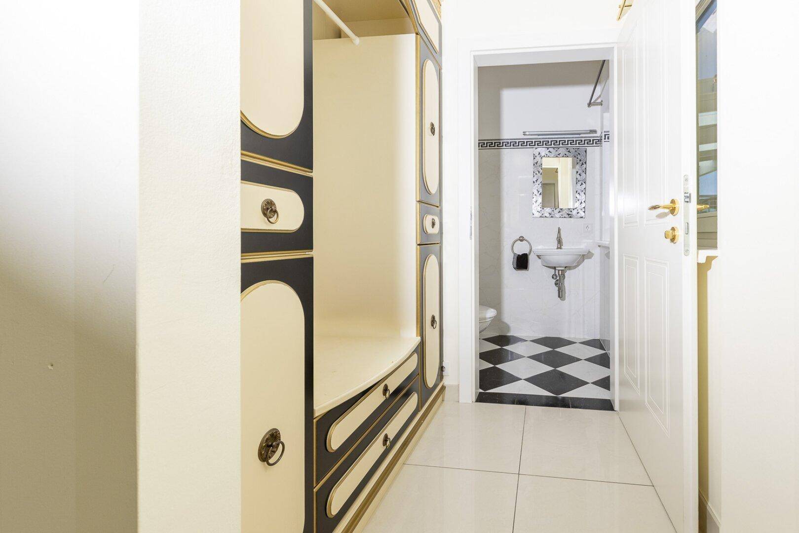 Flur mit Einbauschrank und Blick in ein kleines Badezimmer mit schwarz-weißem Fliesenboden.