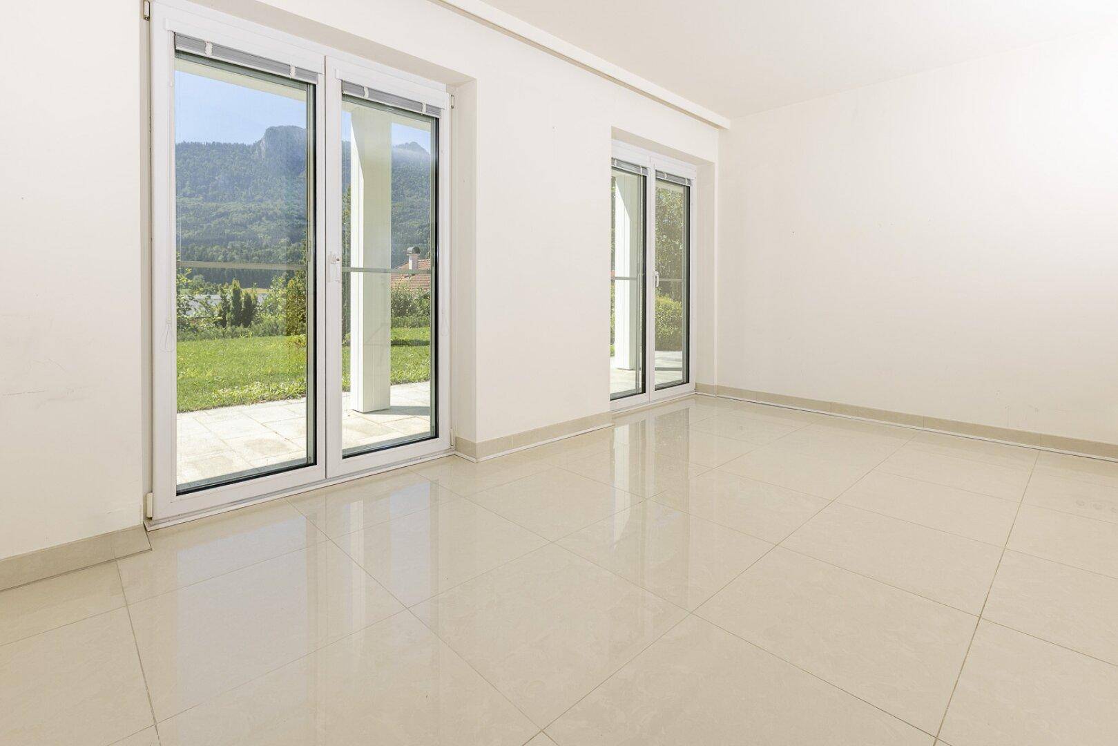 Heller, leerer Raum mit glänzenden Fliesenböden und großen Fenstern mit Blick ins Grüne.