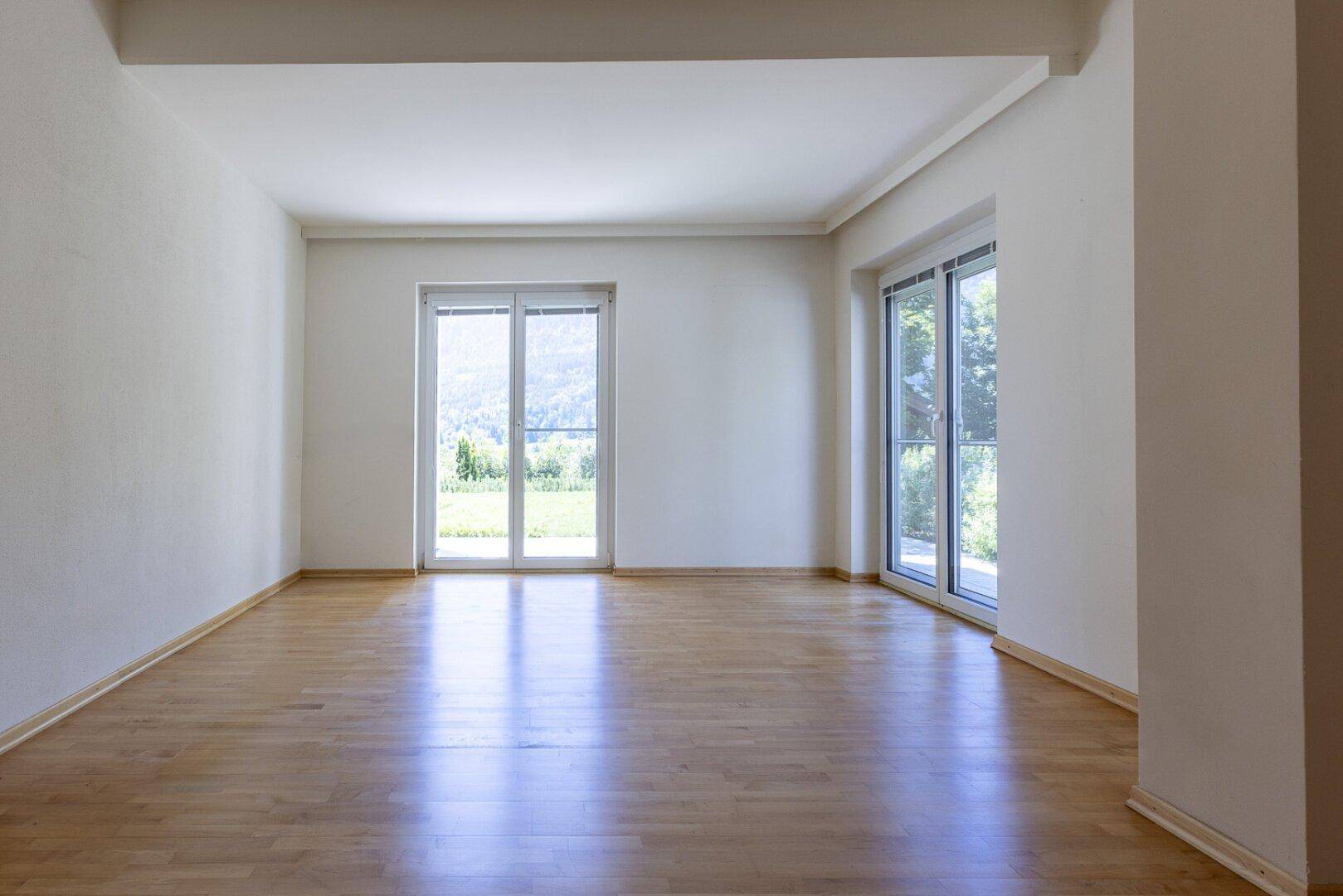 Geräumiger, heller Raum mit Holzboden und großen Fenstern, die viel Tageslicht hereinlassen.