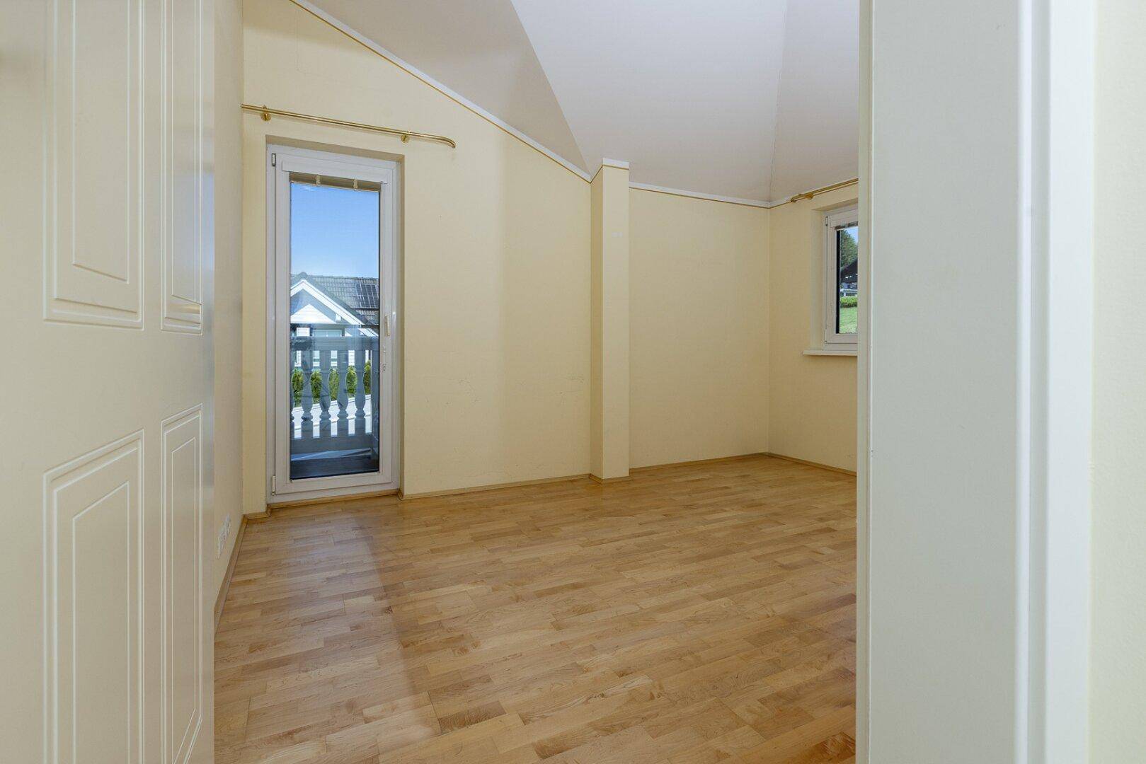 Gemütliches Zimmer mit Holzboden und Zugang zu einem kleinen Balkon, ideal als Schlaf- oder Gästezimmer.