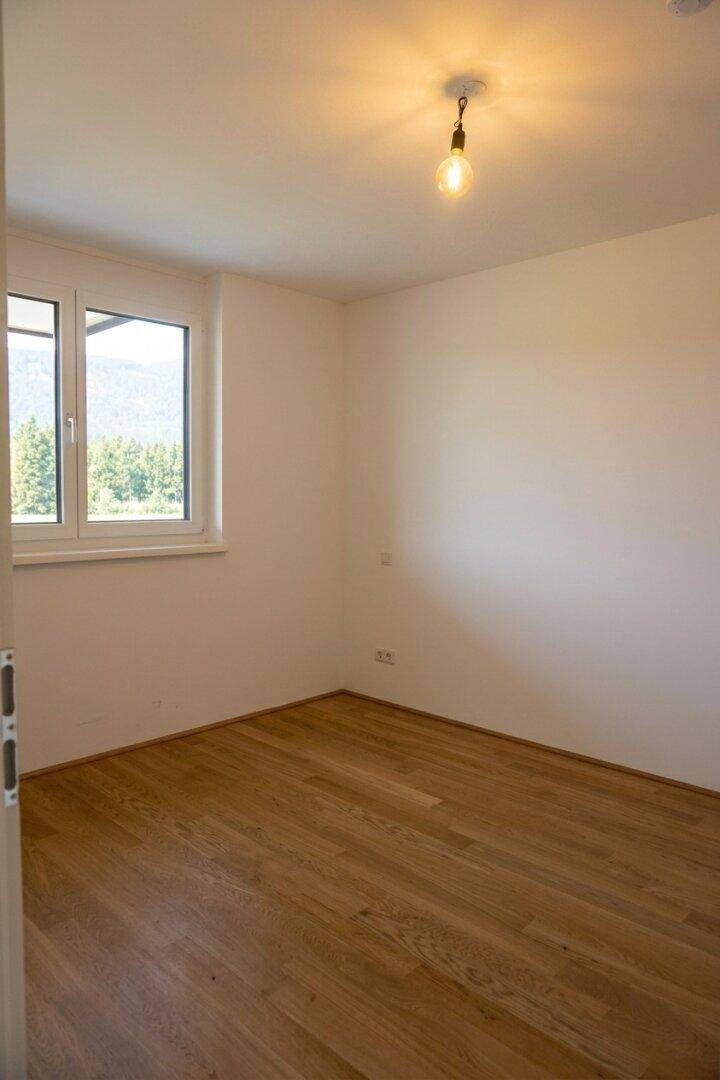 Ruhiges Schlafzimmer mit Holzfußboden und Fenster, das einen schönen Blick ins Grüne bietet.