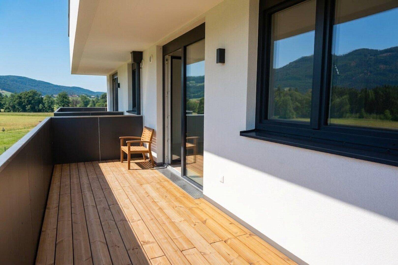 Geräumiger Balkon mit Holzboden und weitem Blick auf die grüne Landschaft und Berge.