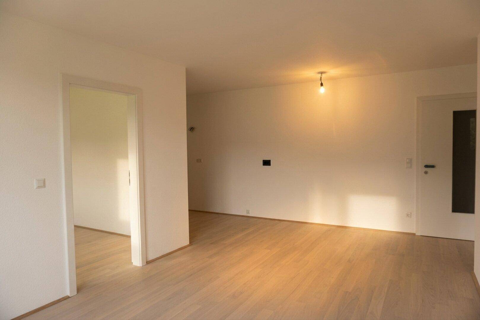 Geräumiger, heller Wohnbereich mit hellem Holzboden und Zugang zu weiteren Räumen.