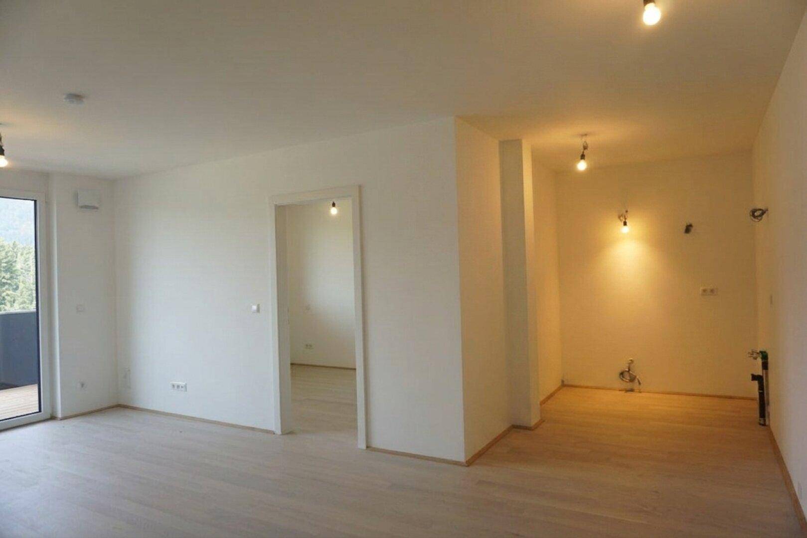 Heller, unmöblierter Wohnbereich mit hellem Holzboden und Zugang zu einem Balkon.