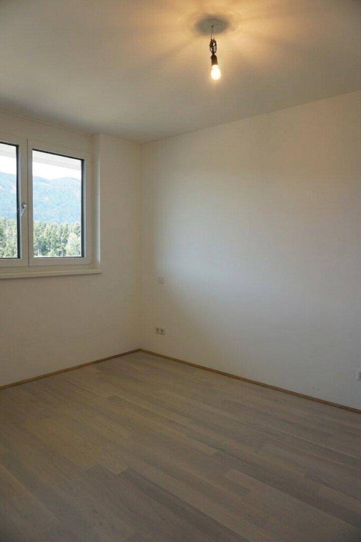 Helles Schlafzimmer mit Holzboden und Fenster, das einen Blick auf die Berge bietet.