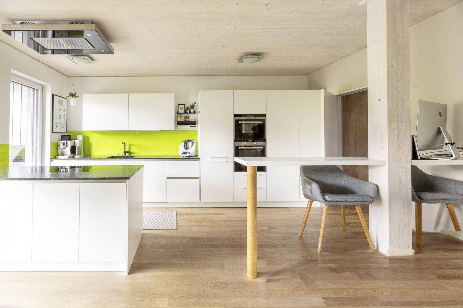 Moderne weiße Küche mit Kücheninsel, integrierten Geräten und hellem Holzboden.