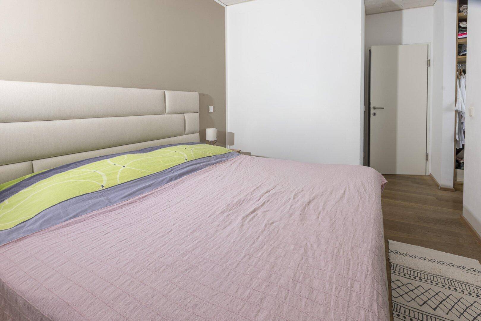 Schlafzimmer mit großem Bett, hellem Holzboden und schlichter Wandgestaltung.