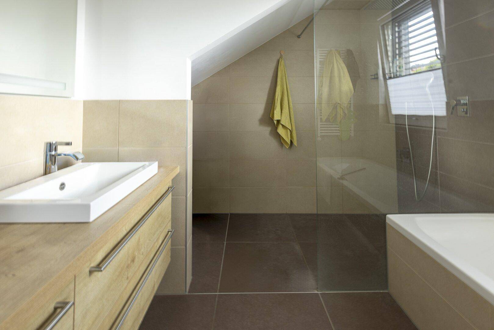 Modernes Badezimmer mit Dusche, Badewanne, Holzwaschtisch und Dachschräge.