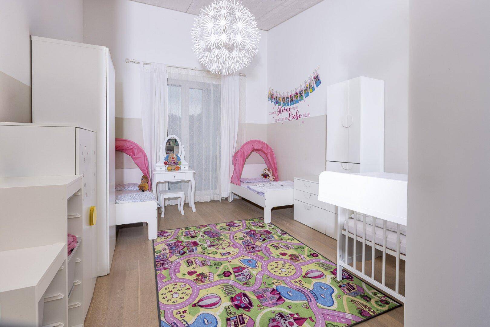Helles Kinderzimmer mit zwei Betten, Wickeltisch und farbenfrohem Teppich.