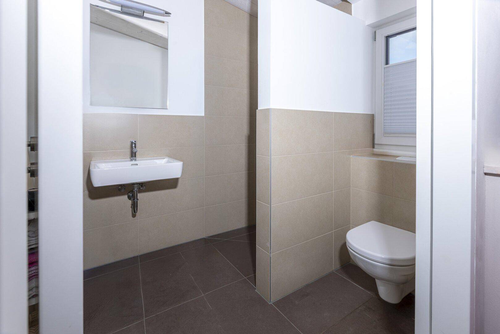 Kleines Gäste-WC mit Fenster, Wand-WC und modernem Waschbecken.