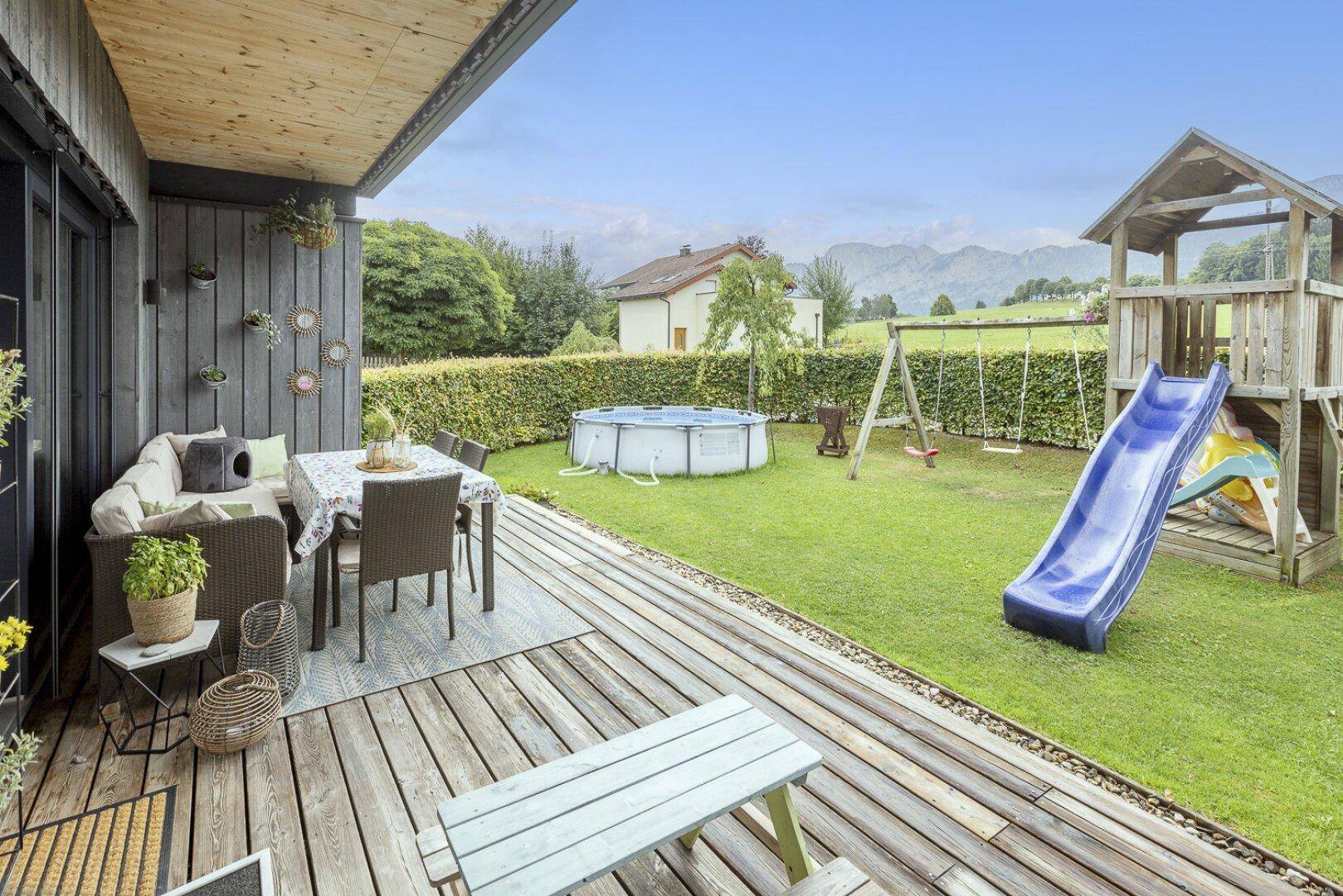 Großer Garten mit Holzterrasse, Spielplatz, Pool und Bergblick.