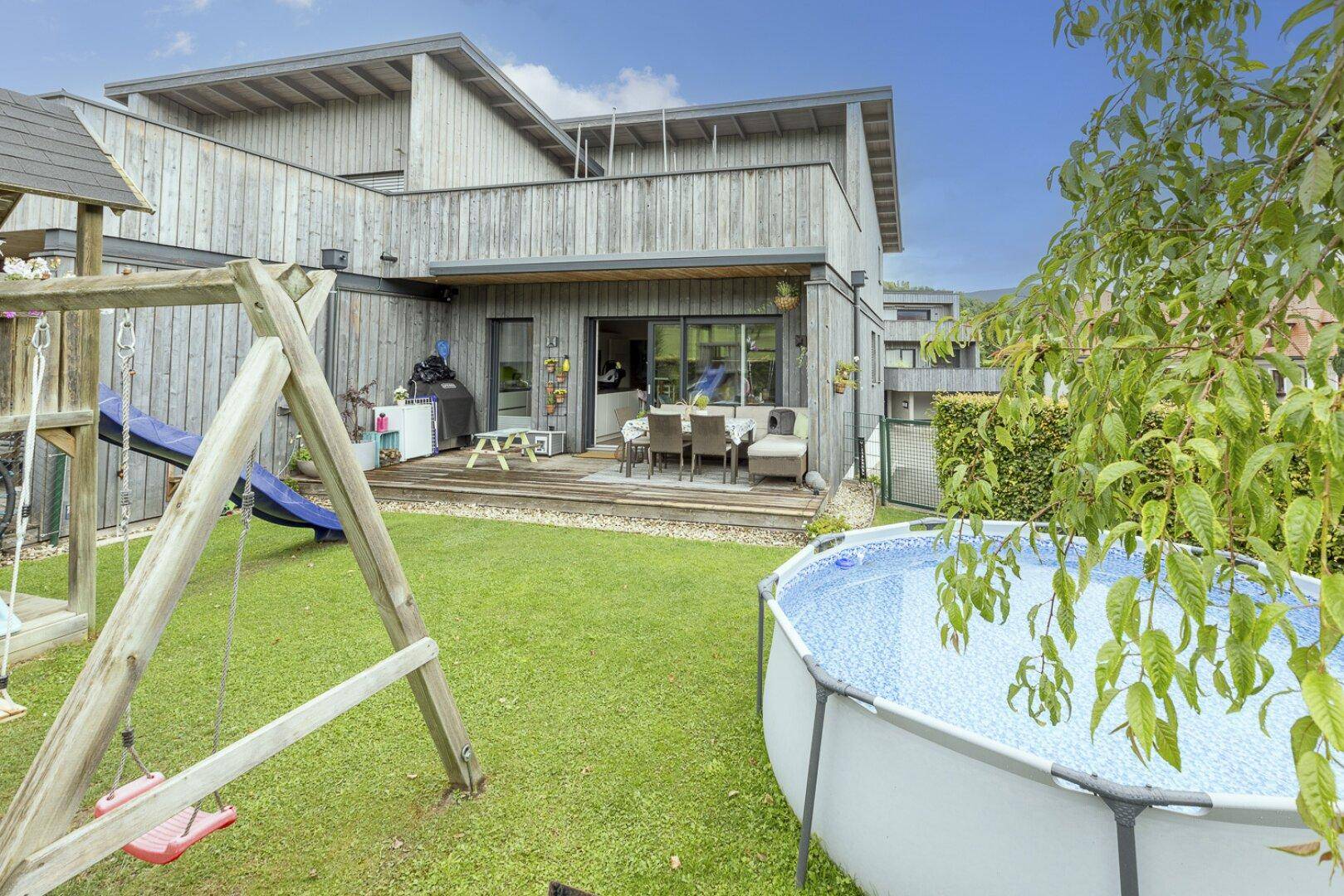 Garten mit Spielplatz, Pool und moderner Holzfassade des Hauses.