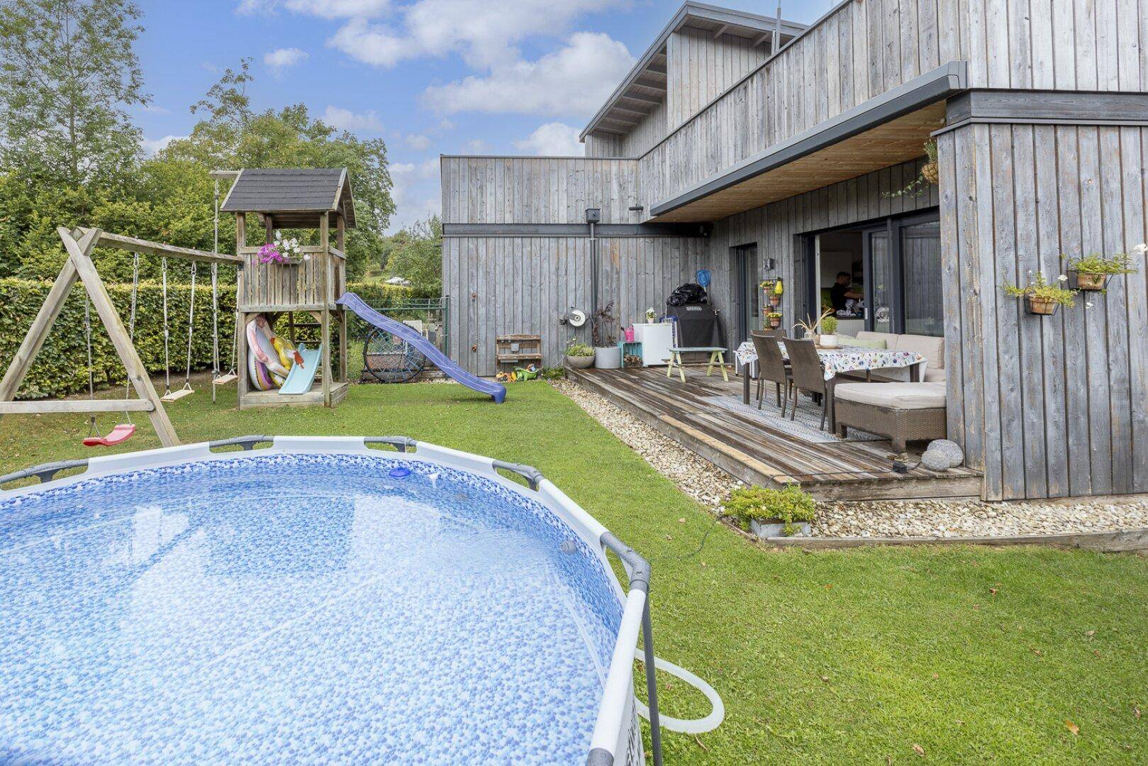 Weitläufiger Garten mit Pool, Spielbereich und Blick auf die Holzfassade des Gebäudes.