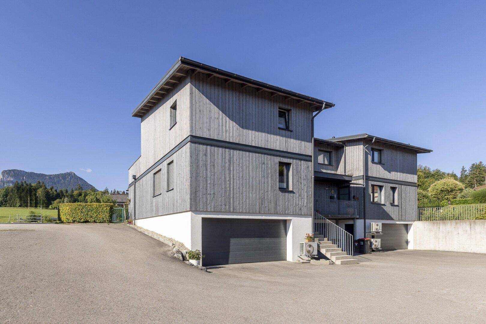 Moderne Wohnanlage mit Holzfassade, Garagen und Bergblick.
