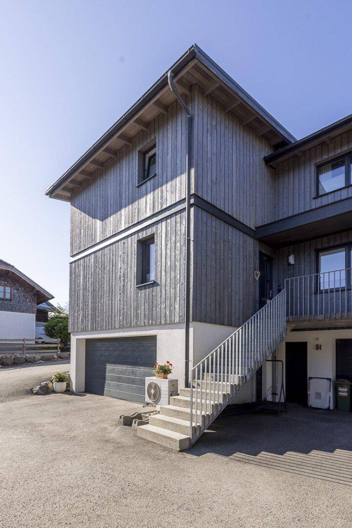 Seitenansicht des Gebäudes mit Holzfassade, Garage und Zugangstreppe.