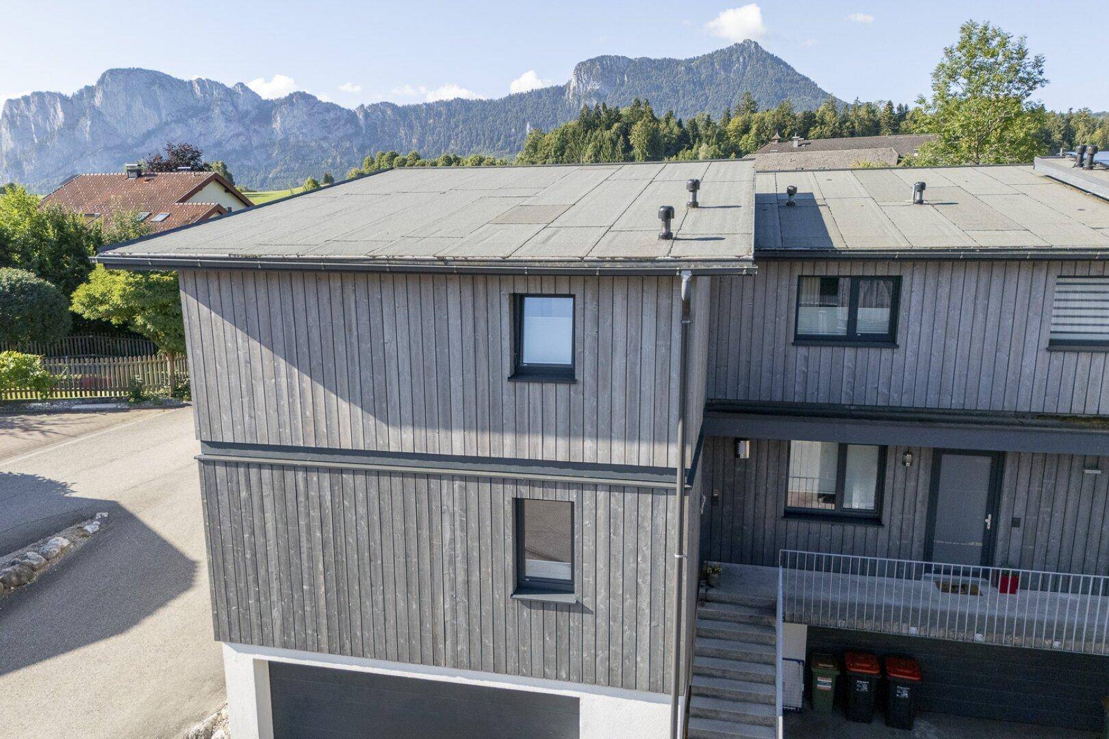 Ansicht des modernen Hauses mit Holzfassade und Bergblick im Hintergrund.