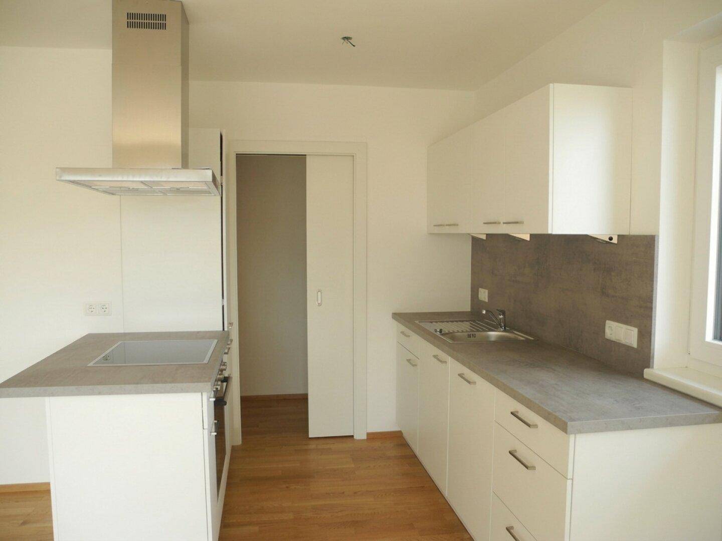 Helle, moderne Einbauküche mit weißen Schränken, grauer Arbeitsplatte und Holzboden.