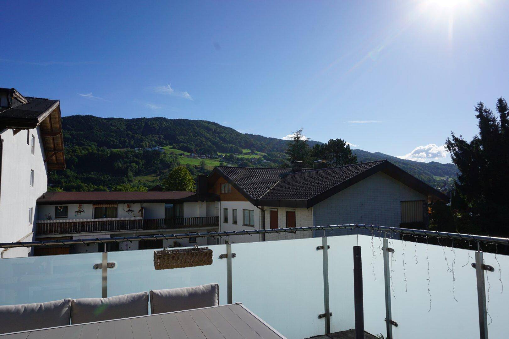 Panoramablick von der Terrasse auf die grüne Berglandschaft unter blauem Himmel.