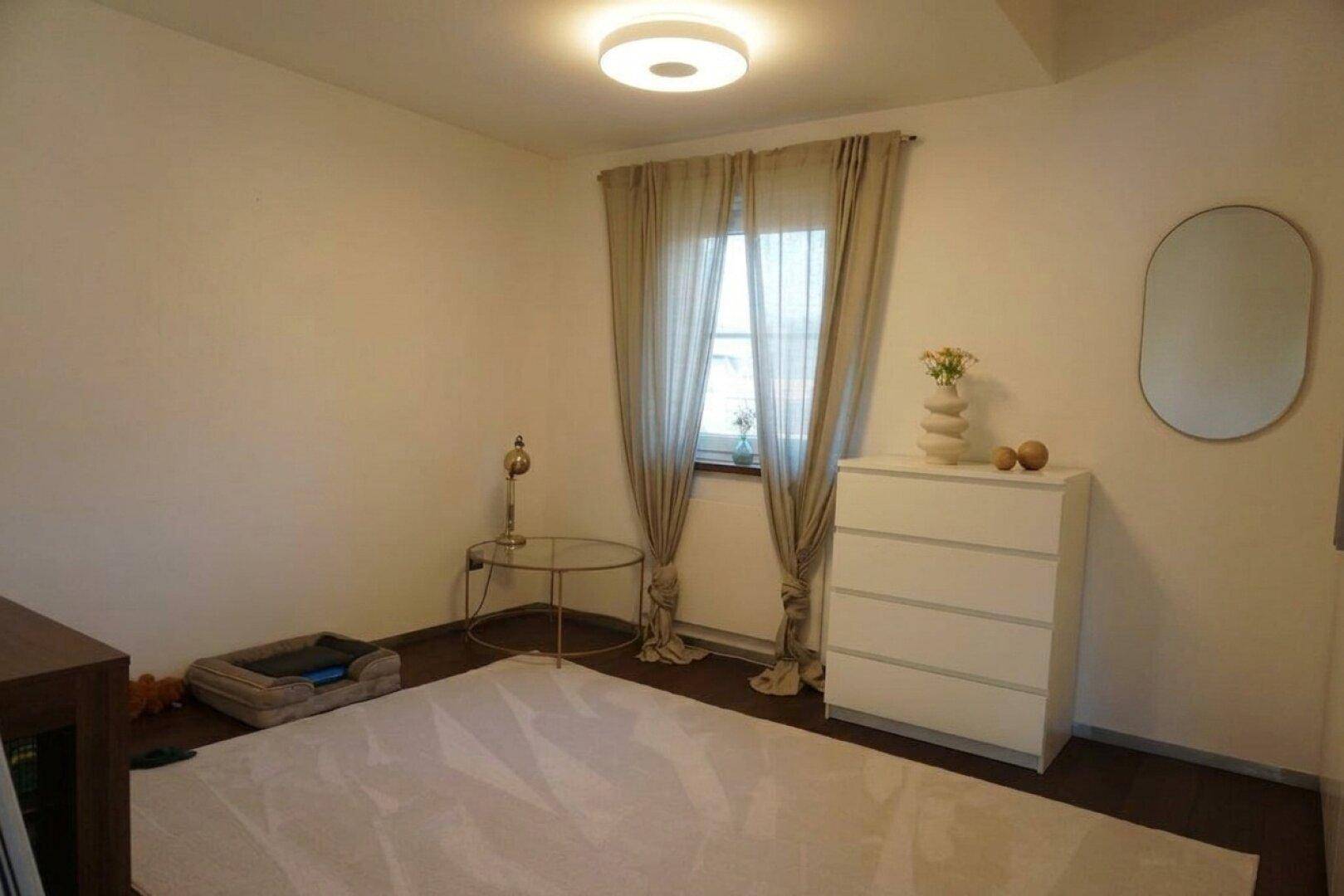 Ruhiges Schlafzimmer mit Laminatboden, Kommode und Fenster.