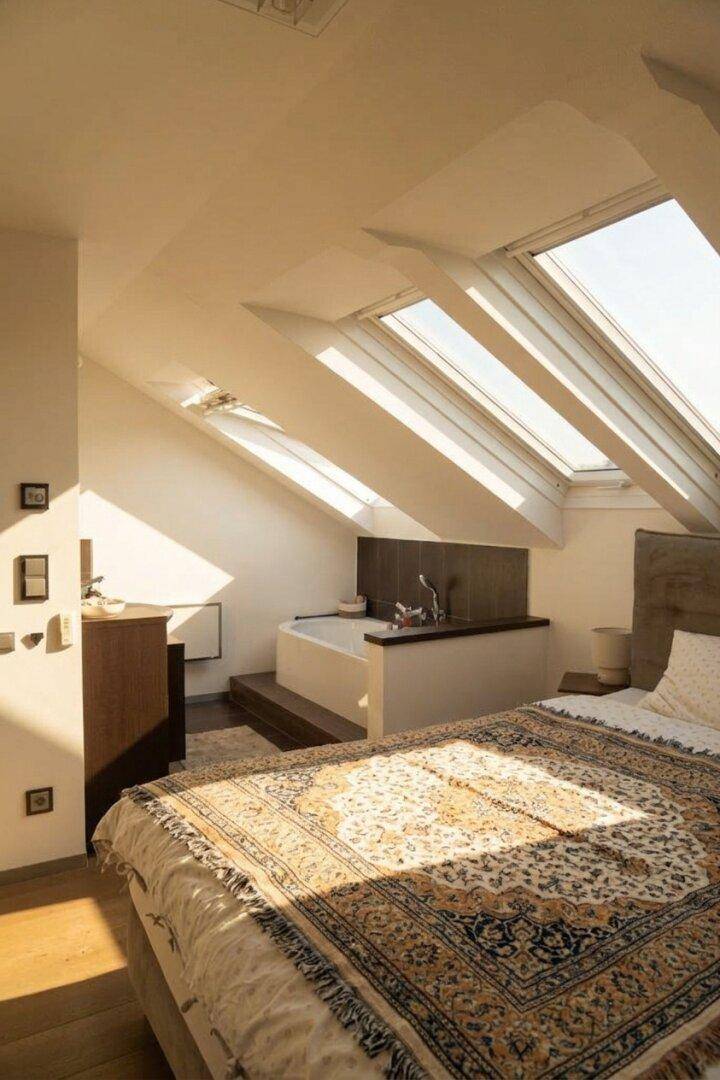 Helles Schlafzimmer im Dachgeschoss mit vielen Dachfenstern und integrierter Badewanne.